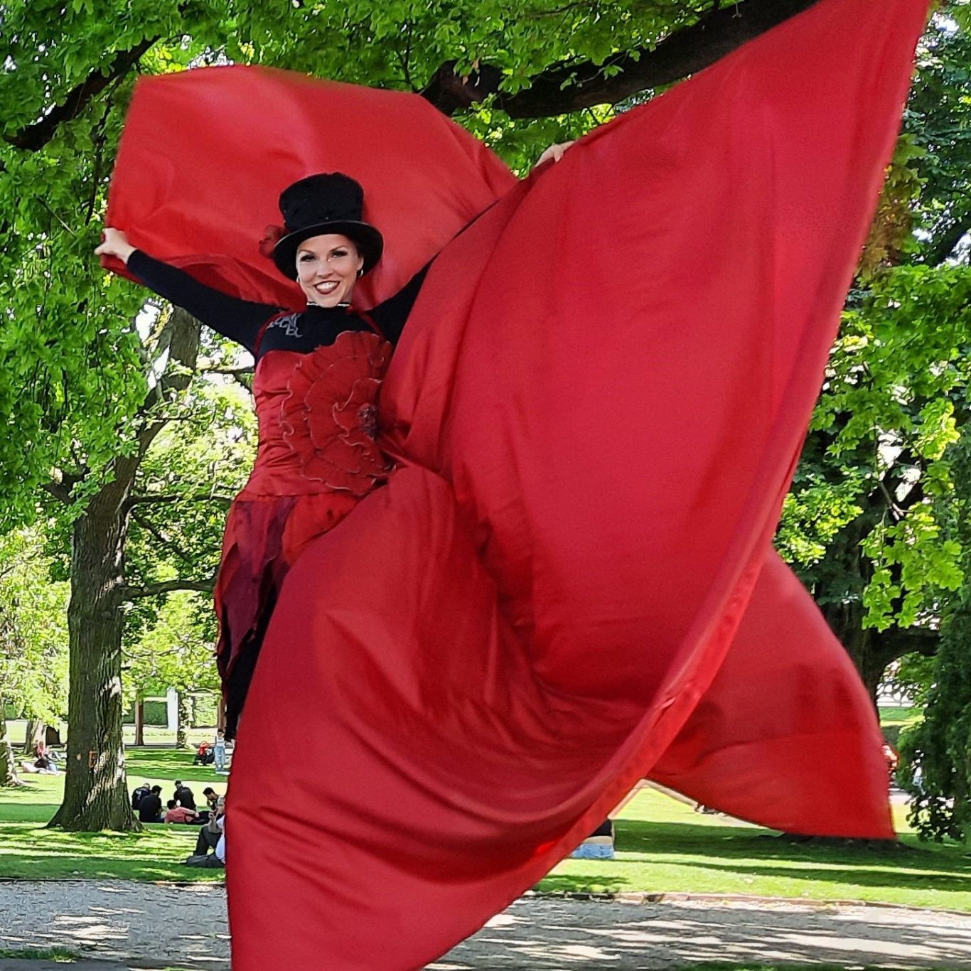 Stelzentheater - Stelzenläuferin einem roten Kostüm unter Bäumen auf einem Parkfest.